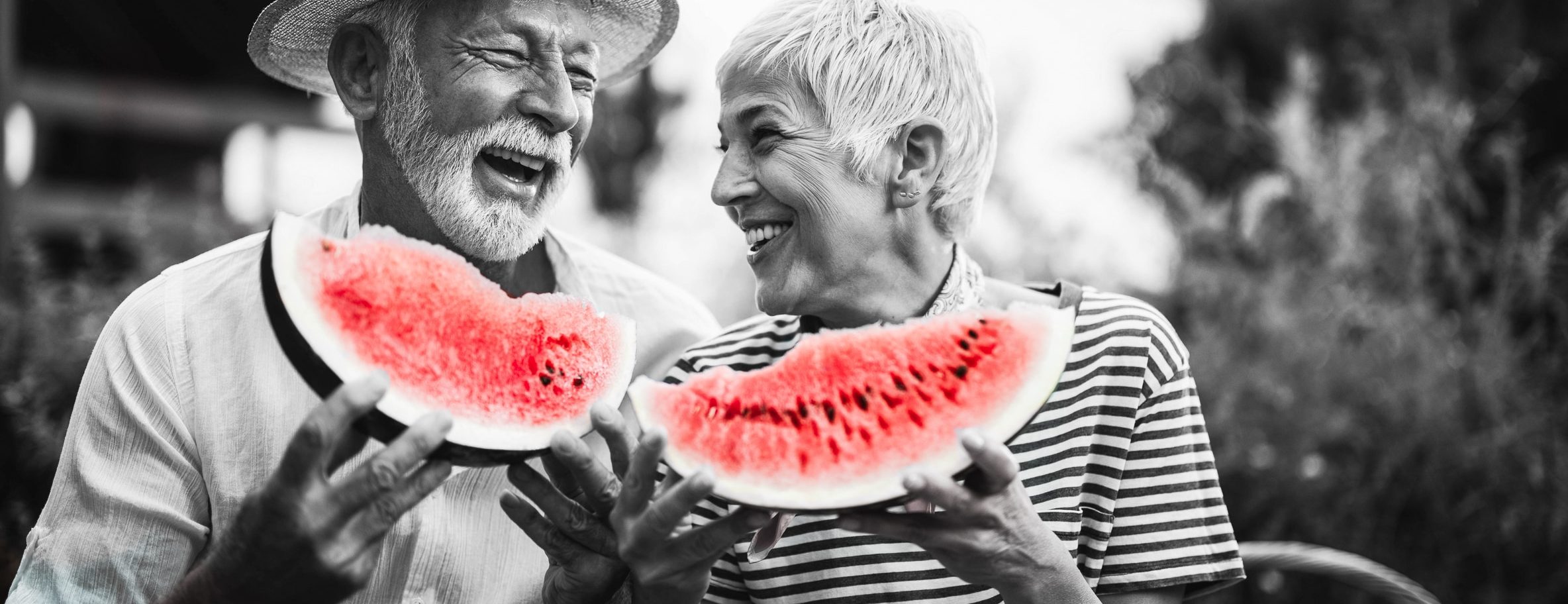 Healthy elderly couple sit outside, laughing and eating fruit