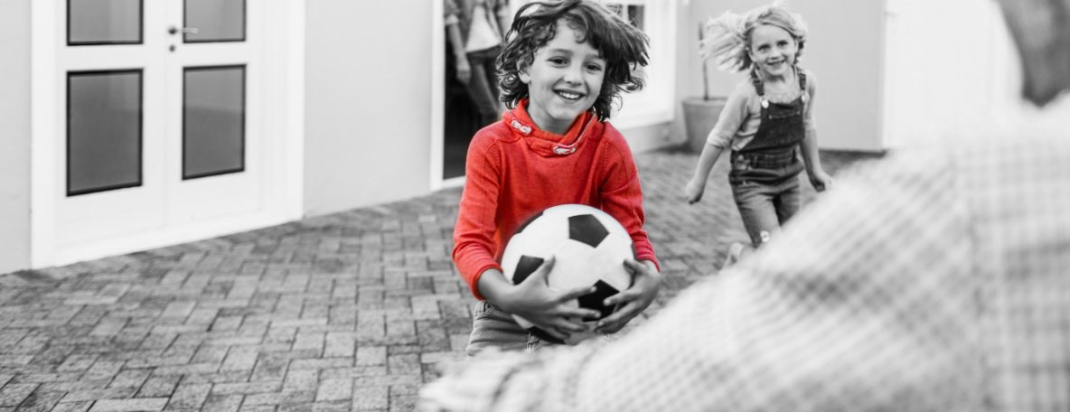 An Australian father's son and daughter run up to him excitedly with a soccer ball as he arrives home, with his wife smiling in the background