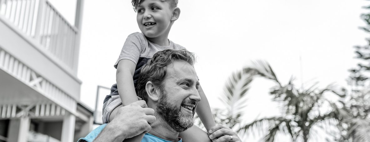 Australian father walks in his backyard while his son happily sits on his shoulders