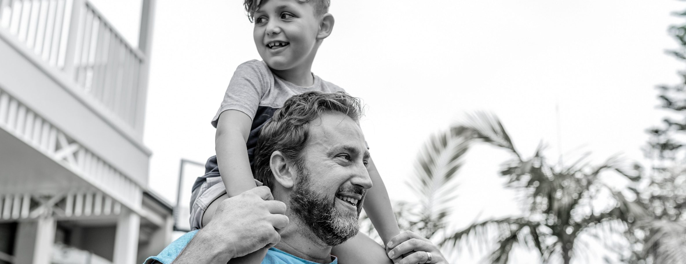 Australian father walks in his backyard while his son happily sits on his shoulders