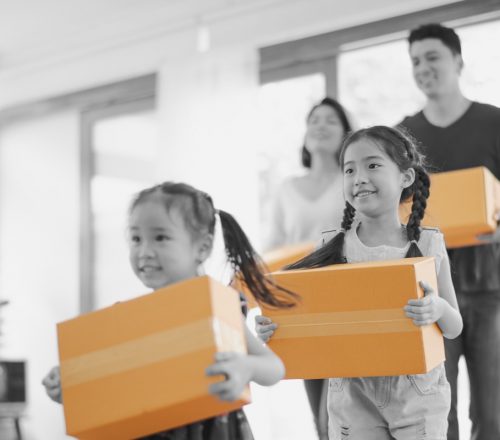 Young Asian family with two daughters run excitedly into their newly bought home with boxes to unpack