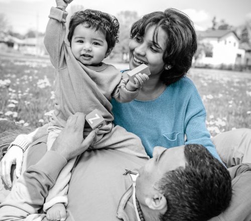 West Asian family lounge in the grass outside, watching on at their young, happy son playing with blocks