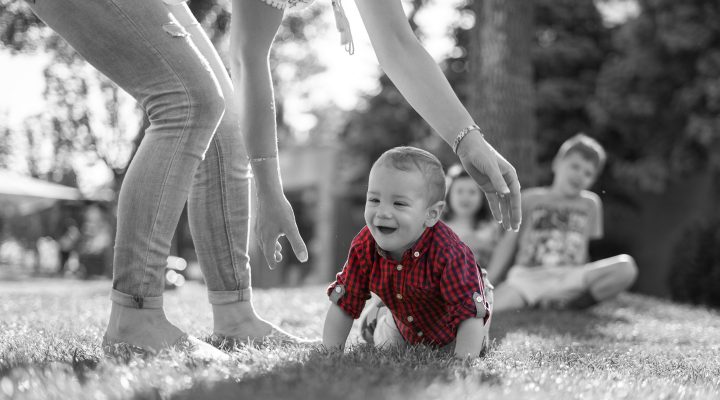A young mother reaches down to guide her newborn who is crawling for the first time