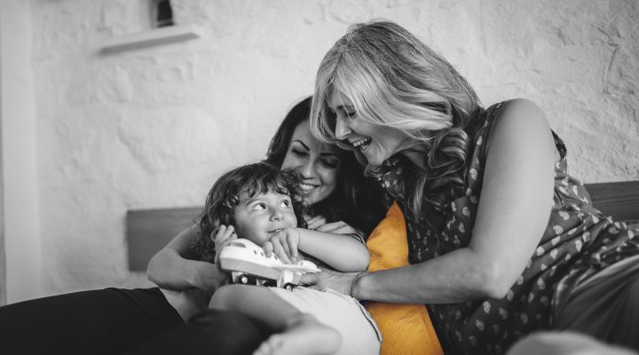 Three generations of a family, sit on a couch, while the grandma and mother coddle the child