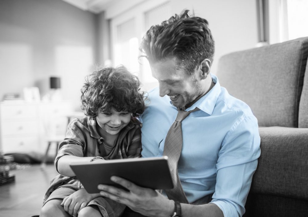 White collar father sits and helps his son complete homework on the tablet