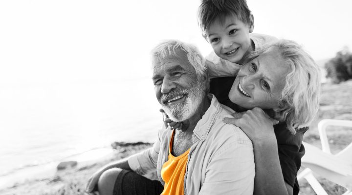 Retired couple sit on an Australian beach as their grandson leans over them